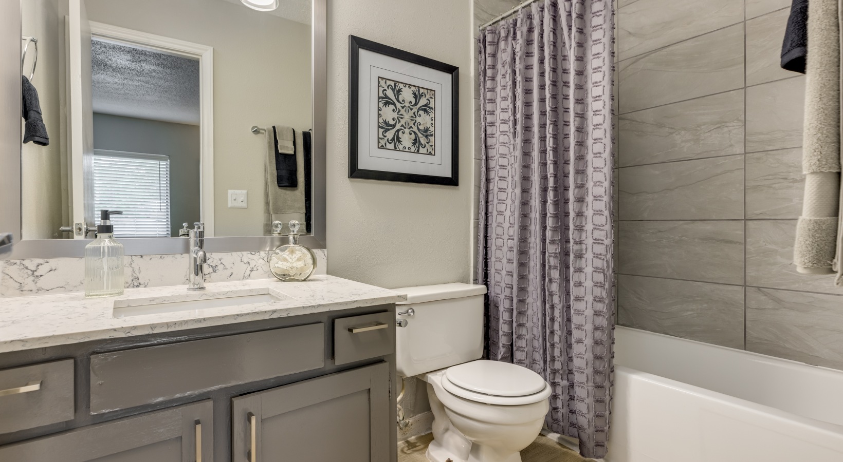 a bathroom with a gray vanity, white cabinets and gray tile at The  Tatum